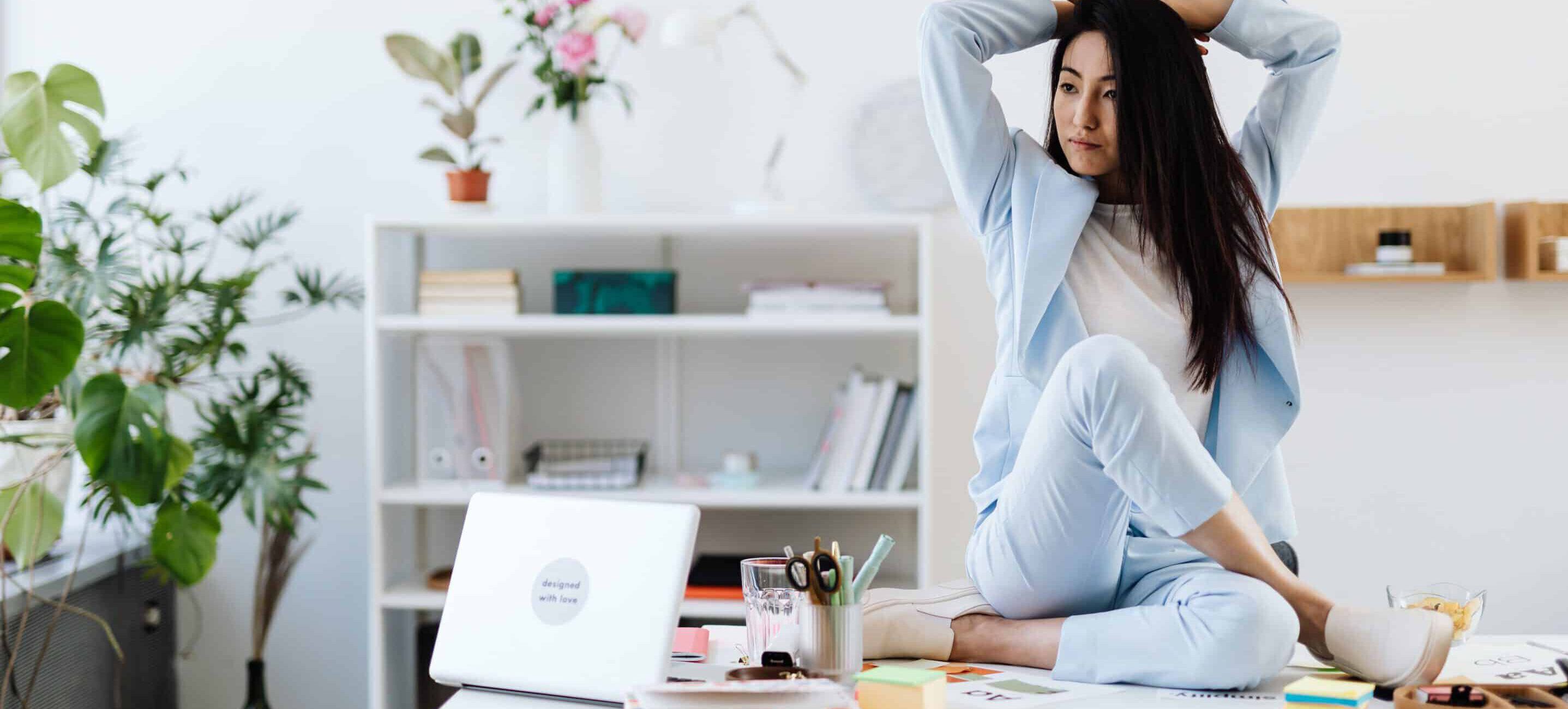 Eine Frau sitzt auf einem Schreibtisch und übt eine Dehnübung aus. Workshop Ergonomie und Bewegung Arbeitsplatz