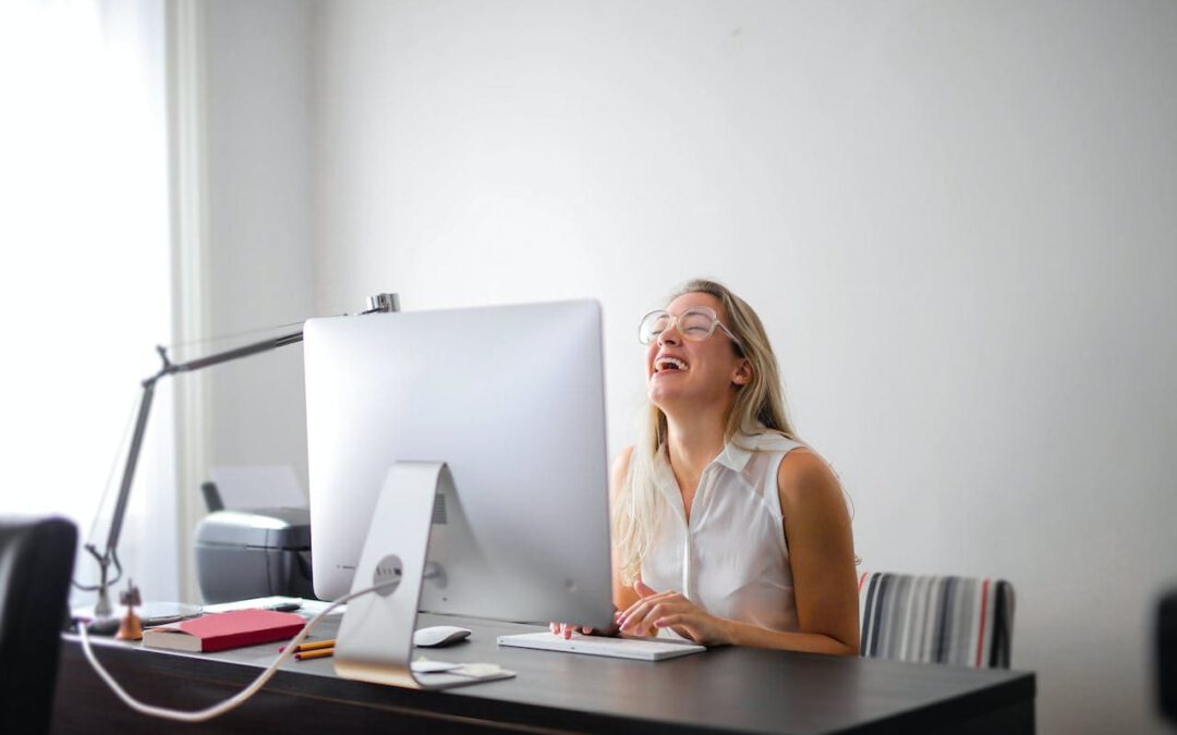 Frau sitzt lachend vor dem Computer am Arbeitsplatz