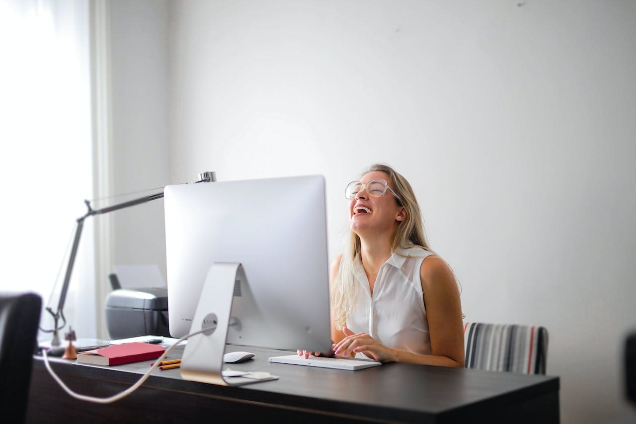 Lachen ist gesund_comp Frau sitzt lachend vor dem Computer am Arbeitsplatz