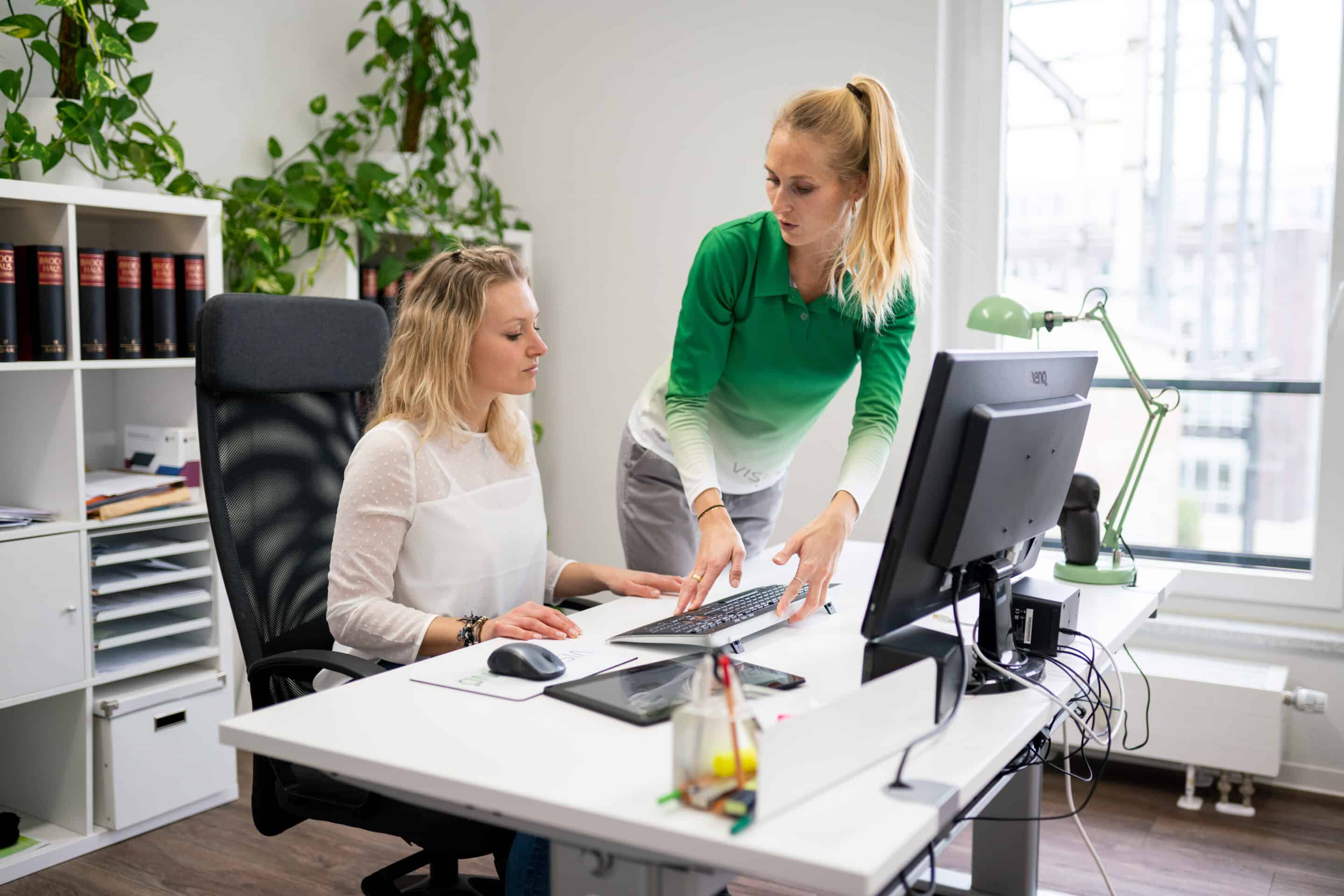 Eine Gesundheitsberaterin spricht im Büro mit einer Mitarbeiterin über ergonomisches oder gesundheitsbezogenes Arbeiten.