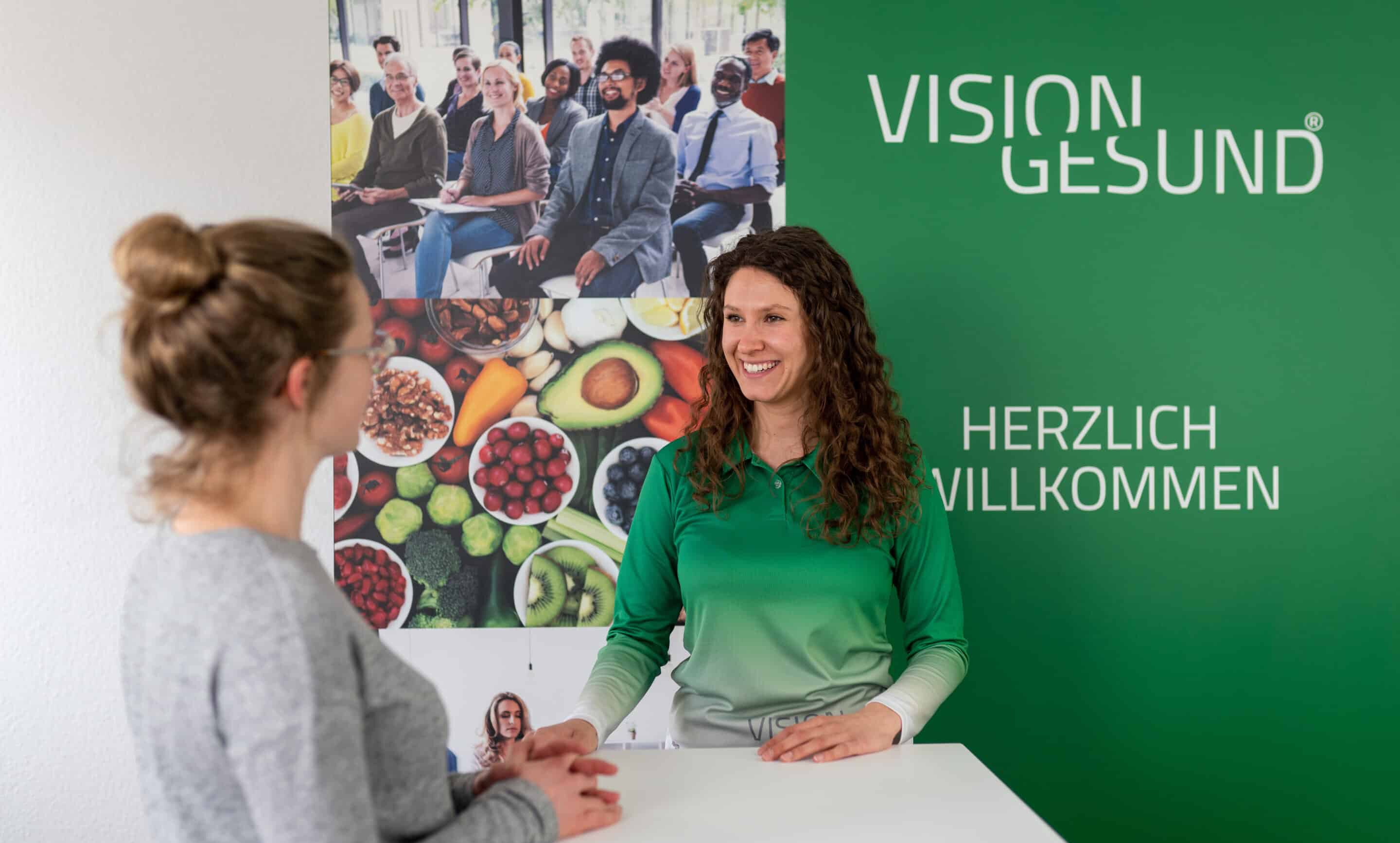 Eine Frau steht hinter einem Tisch und informiert eine Frau über Ihre Gesundheitsangebote.