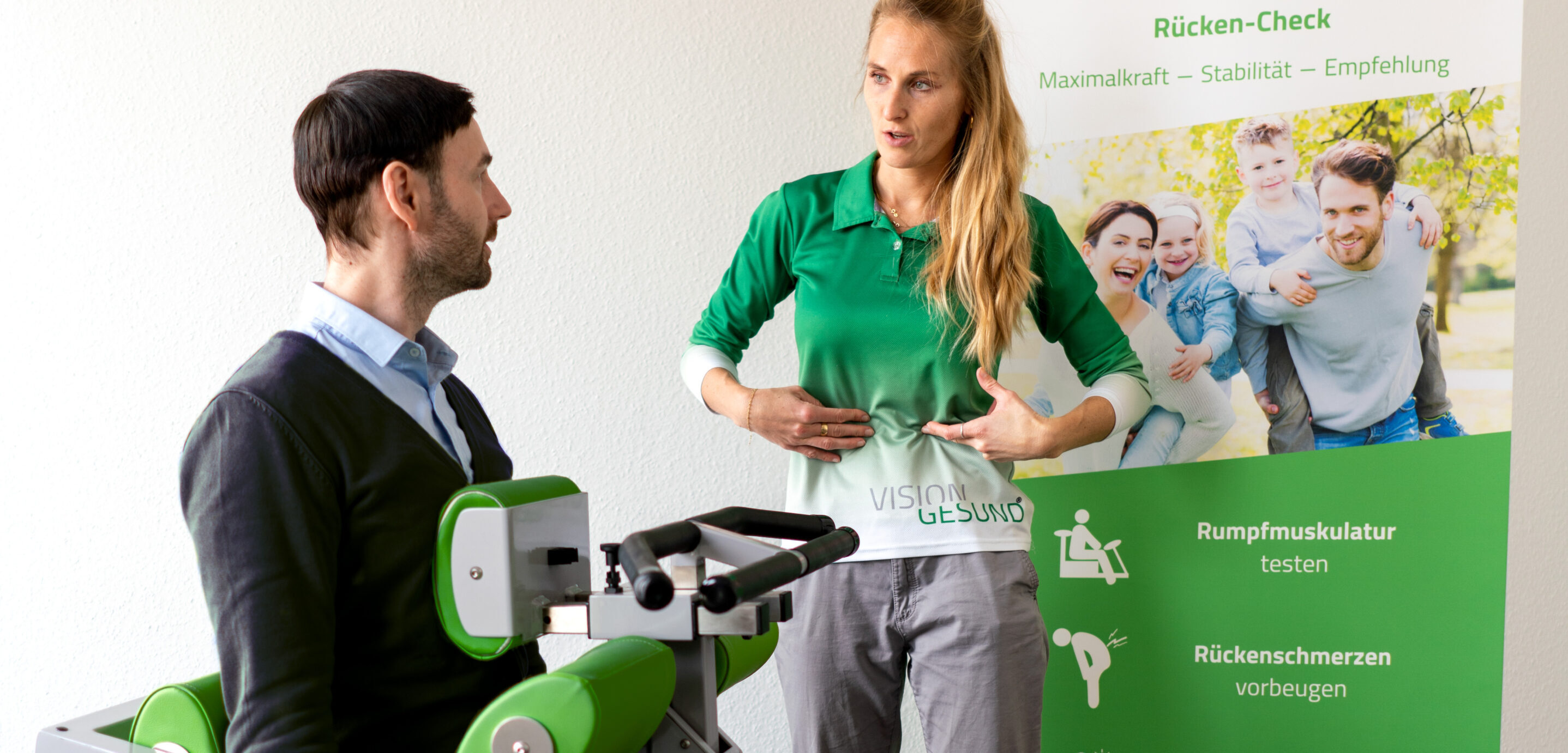 Eine Person nutzt ein diagnostisches Gerät zur Rückenmessung, während eine weitere Person daneben steht. Im Hintergrund sind Informationsbanner zu Rückengesundheit zu sehen.