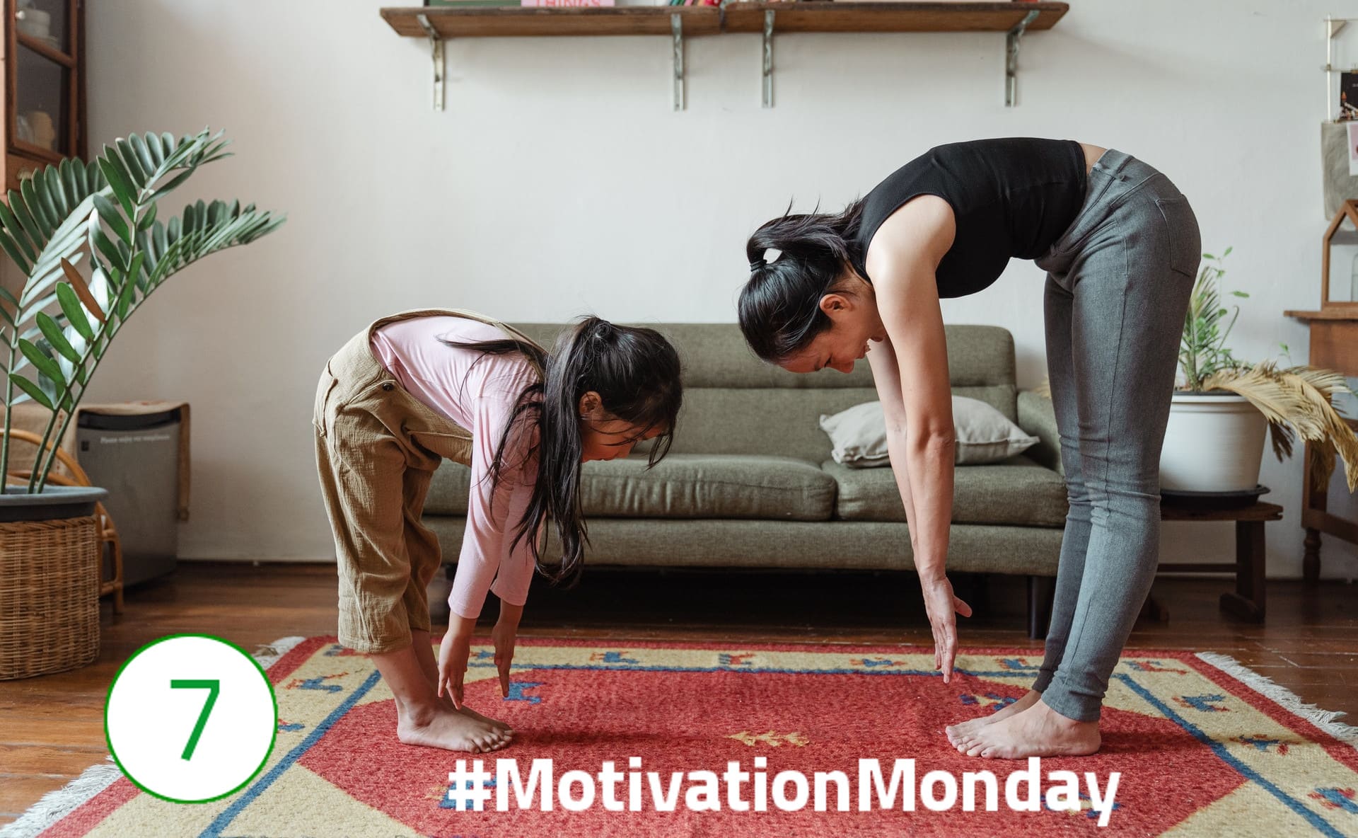 #MondayMotivation – Fürsorge Links im Bild steht ein kleines Mädchen auf einem großen Teppich und bückt sich mit gestreckten Beinen und langen Armen nach vorne. Eine erwachsene Frau steht in der gleichen Position gegenüber; die Arme sind nicht ganz so weit am Boden. Im Hintergrund ist eine Couch zu sehen.