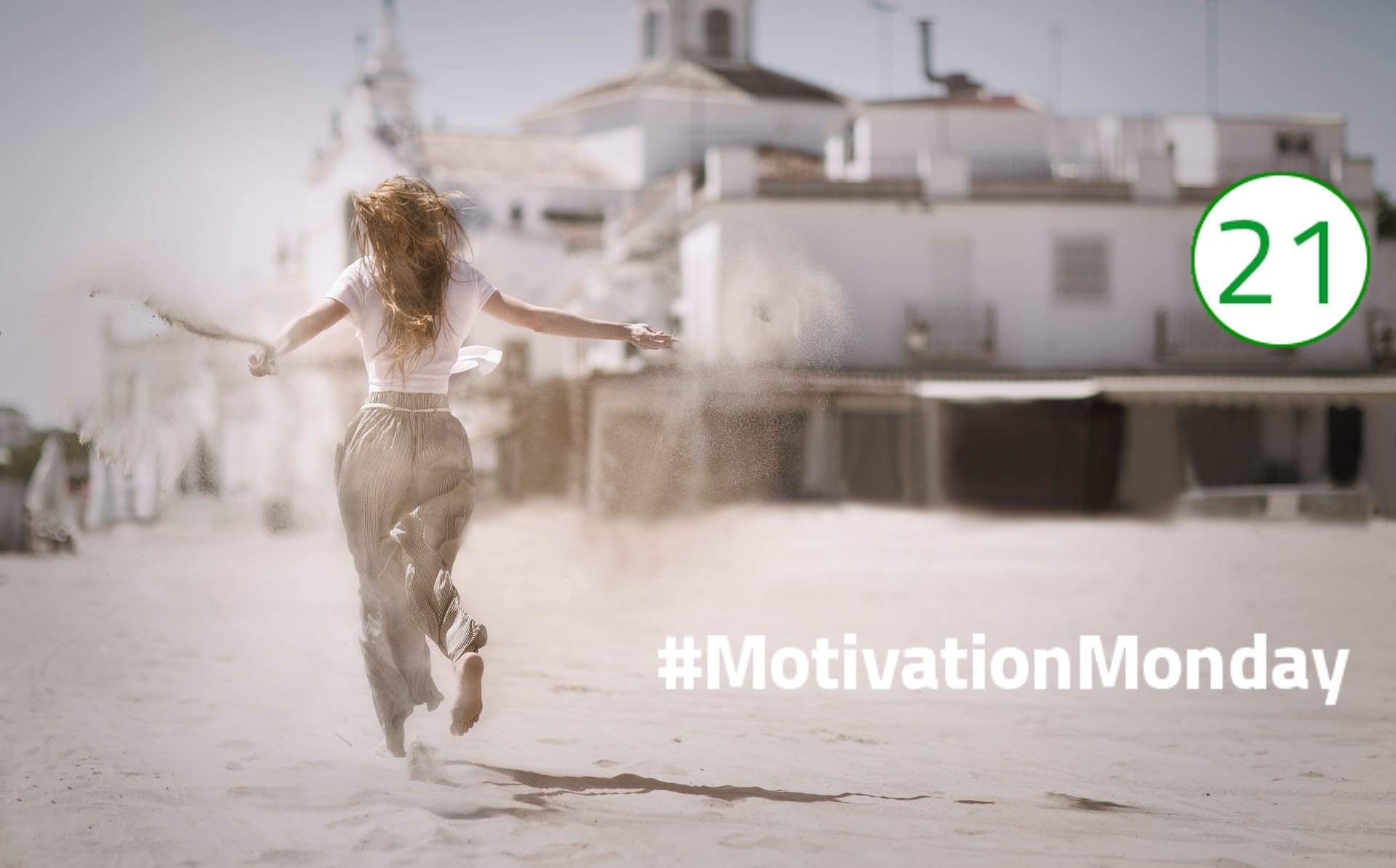 Motivation Monday Sie selbst im Fokus Ihrer Aufmerksamkeit Eine Frau läuft mit ausgebreiteten Armen in einer weiten Haremshose und einem weißen Tshirt auf Sand an einem weißen Häuserkomplex vorbei. Der Sand weht hinter ihr auf, ihre langen braunen Haaren wehen ebenfalls im Wind. Das Bild vermittelt ein Gefühl von Freiheit und Glück.
