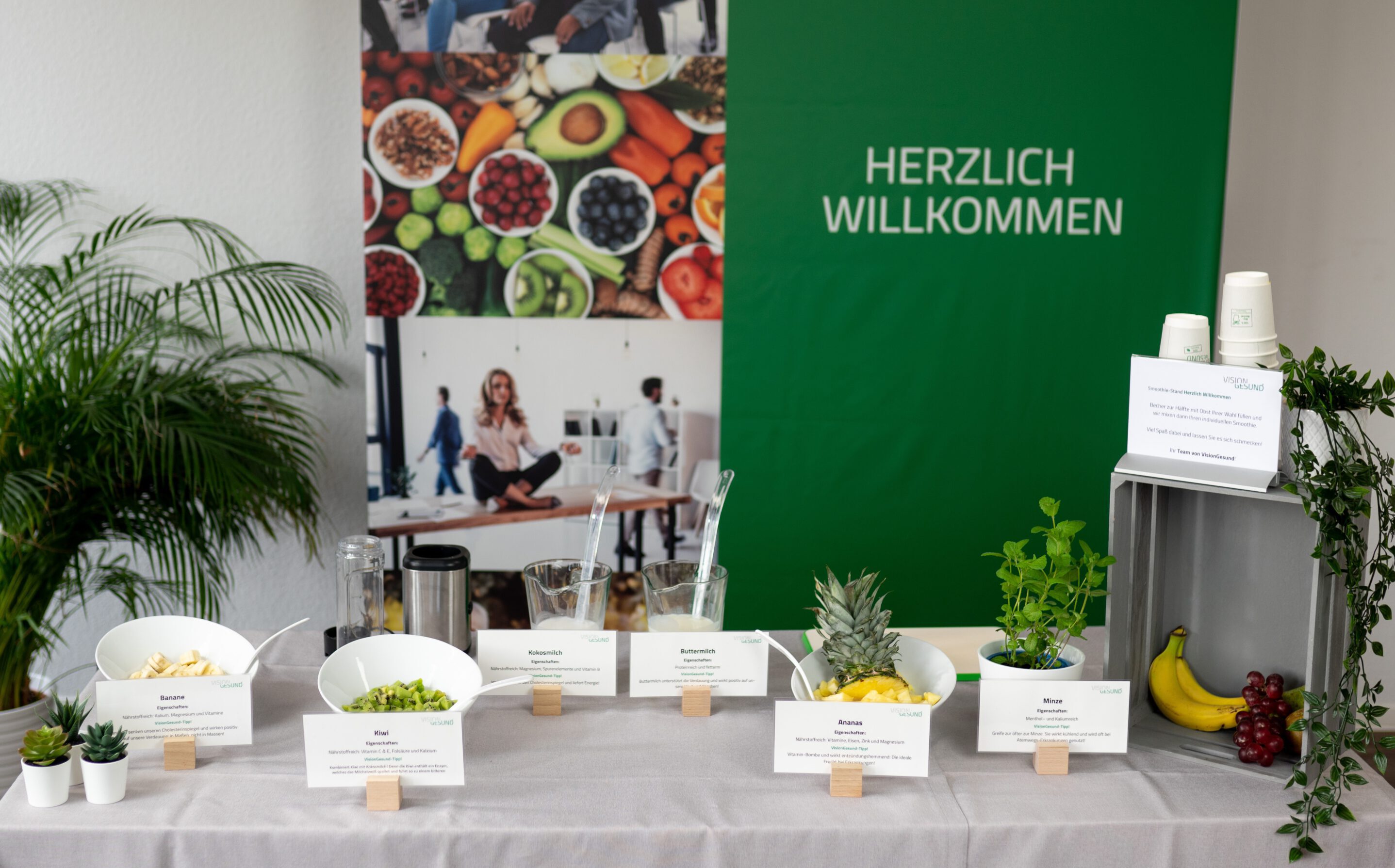 Workshop Gesunde Ernährung Ein einladend dekorierter Tisch mit frischem Obst, Gemüse und Kräutern vor einem grünen „Herzlich Willkommen“-Banner, arrangiert als gesundes Snack‑ oder Infobuffet.