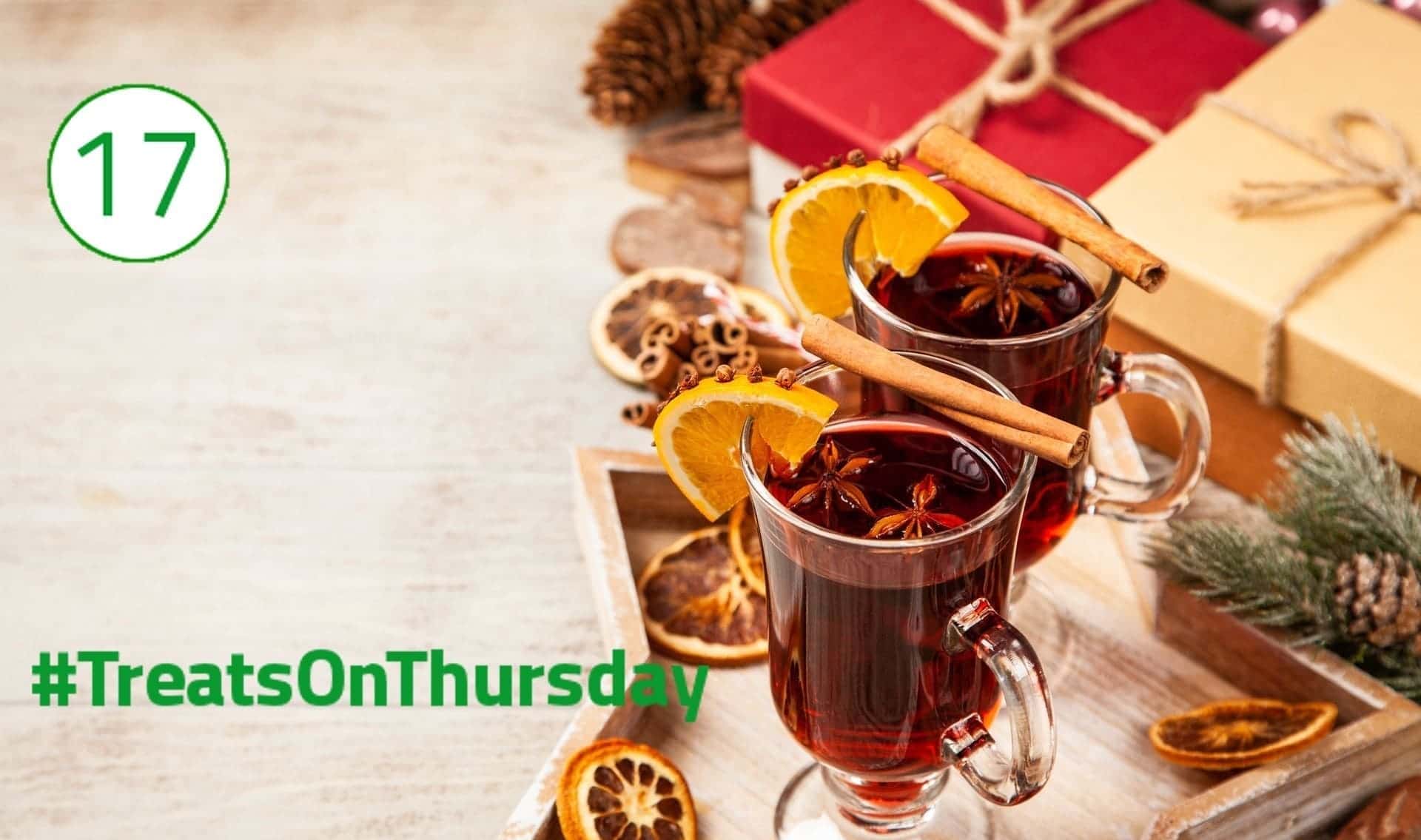 Glühwein #TreatsOnThursay In der rechten Hälfte stehen zwei Gläser gefüllt mit Glühwein. Auf ihnen liegen jeweils eine Zimtstange und eine Orangenscheibe, in der Nelken stecken. Im Glas schwimmt ein Anisstern. Im Hintergrund liegen verpackte Geschenke.
