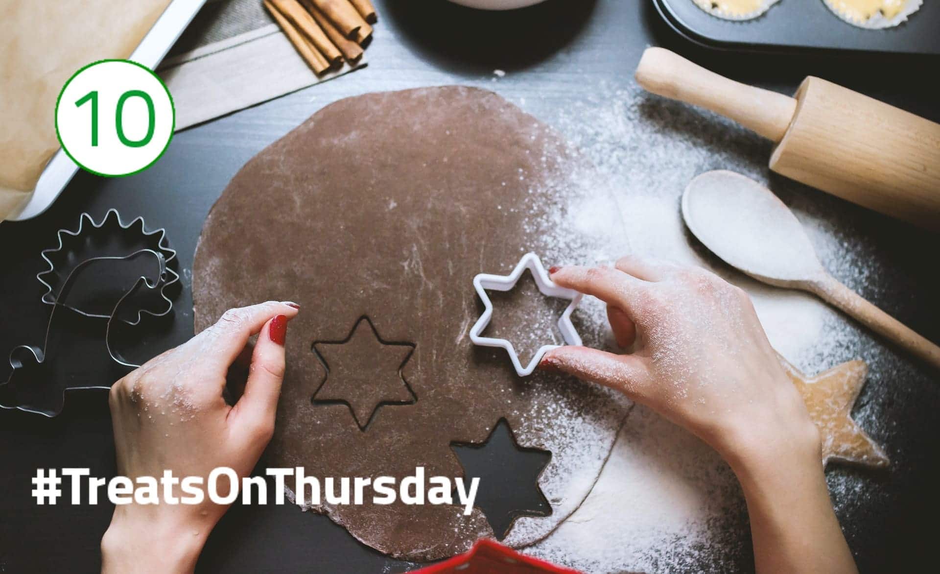 #TreatsOnThursday – Plätzchen backen Ein dunkler Plätzchenteig liegt flach und kreisrund ausgerollt auf dem Tisch. Darauf werden kleine Sternchen ausgestochen, drumherum liegen verschiedene Backutensilien.