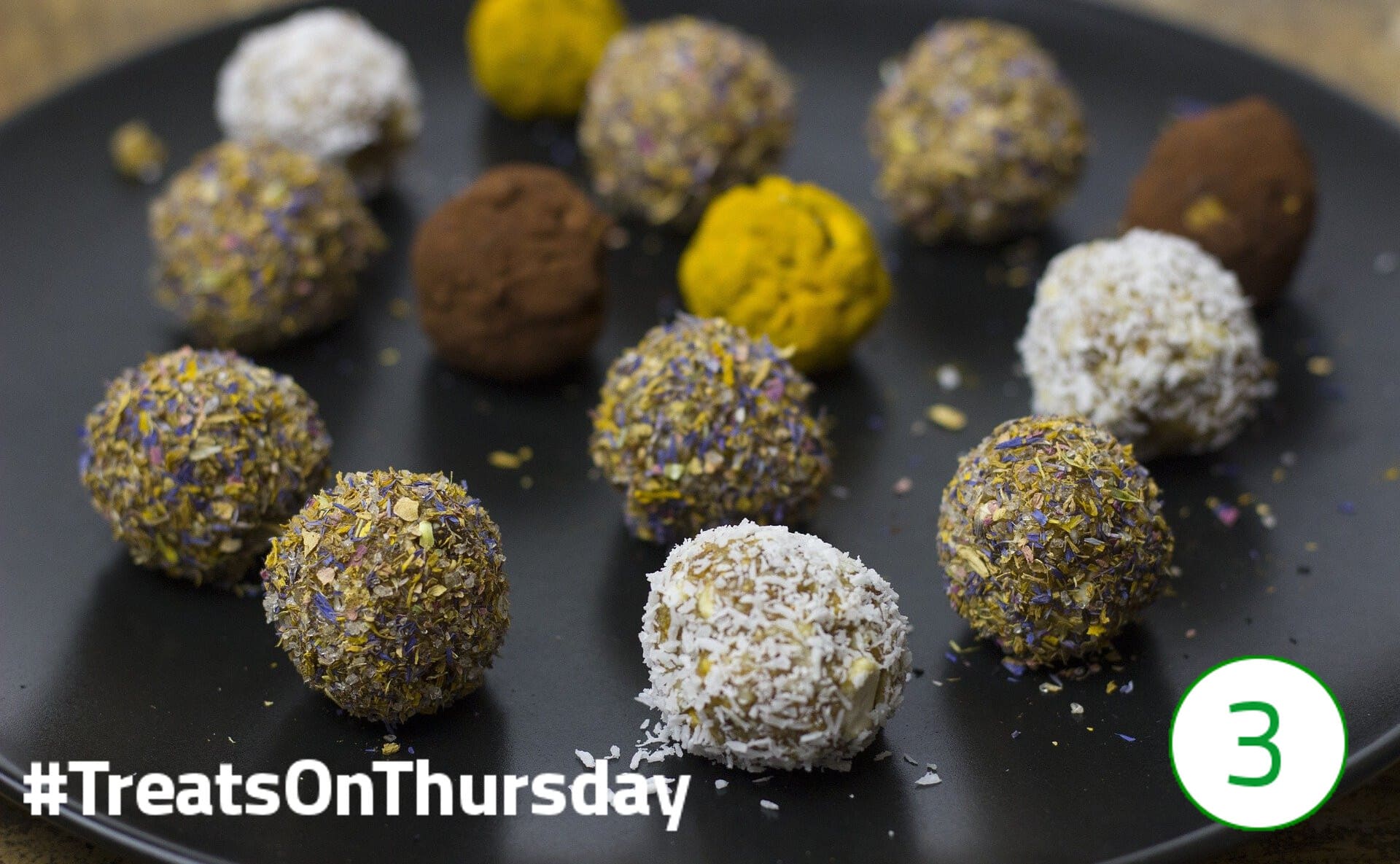 #TreatsOnThursday – Pralinen 14 Pralinenkugeln verschiedener Farben liegen auf einem schwarzen Teller.