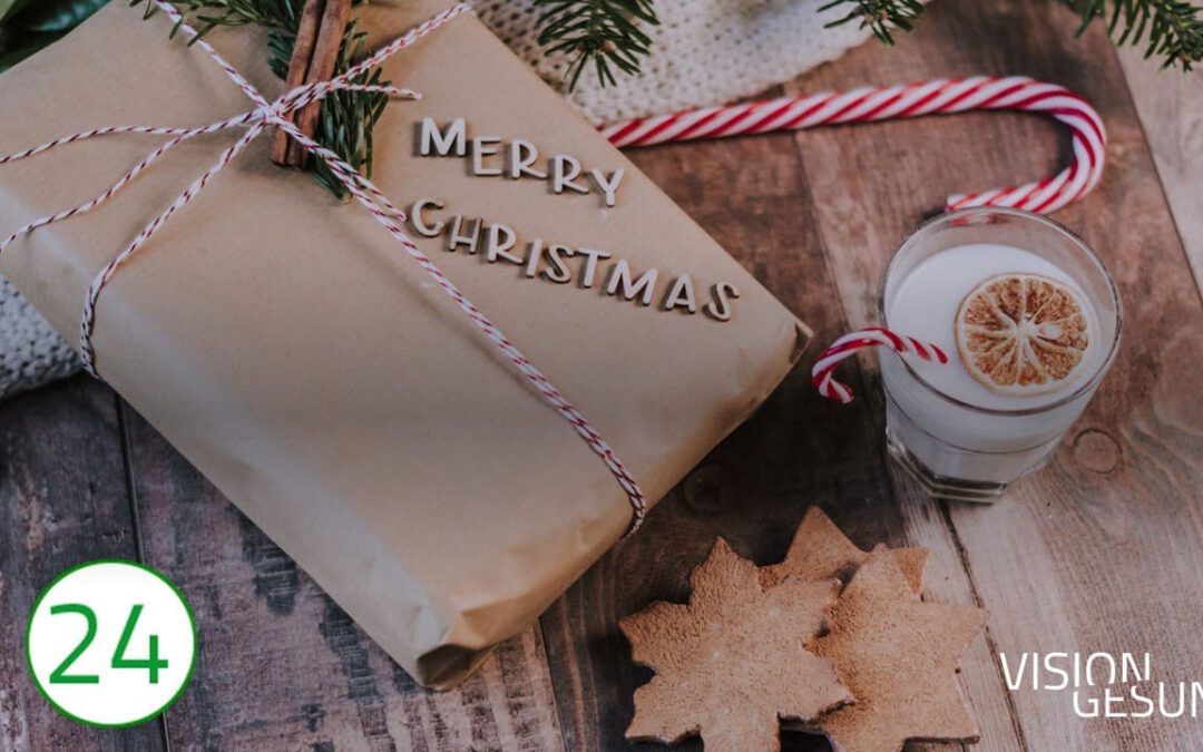 Auf der linken Seite des Bildes liegt ein in Paketpapier geschnürtes Päckchen, um das viele weihnachtliche Dekors wie eine rotweiße Zuckerstange in einem weißen Getränk, Holzsterne, Zimtstangen und Tannenzweige drapiert sind. Den Untergrund bildet ein stilvoller Holztisch. Auf dem Paket prangen die Worte: Merry Christmas.