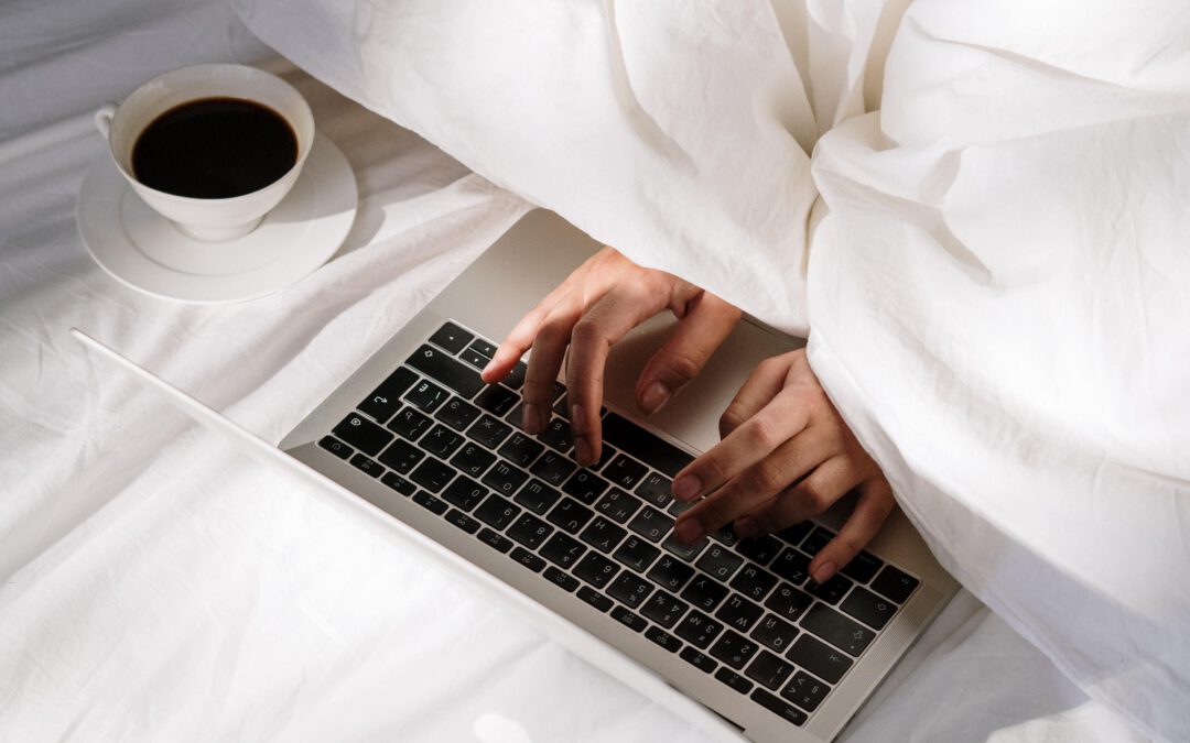 person mit labtop und kaffee halb unter der bettdecke